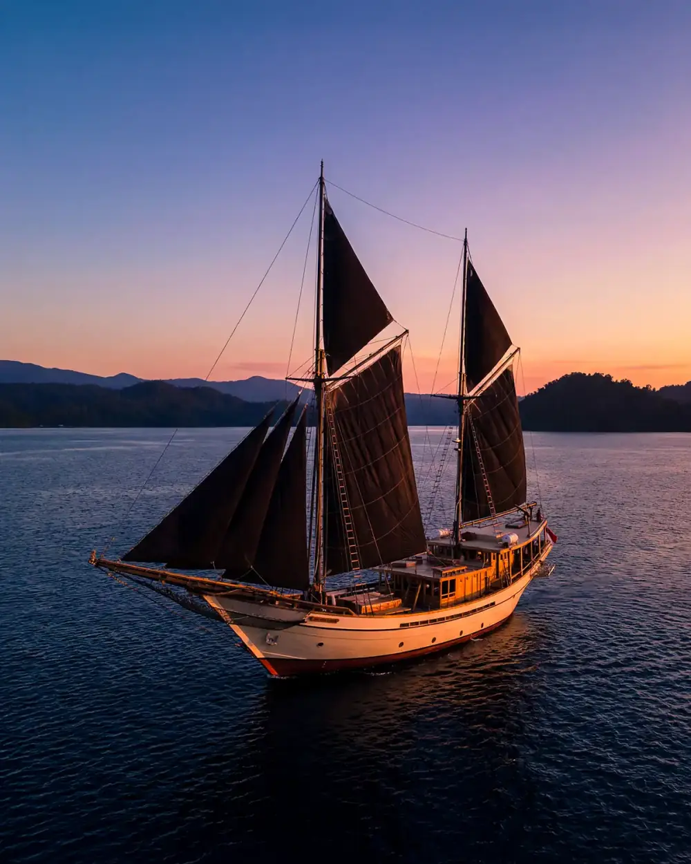 Phinisi with dark sails at dusk