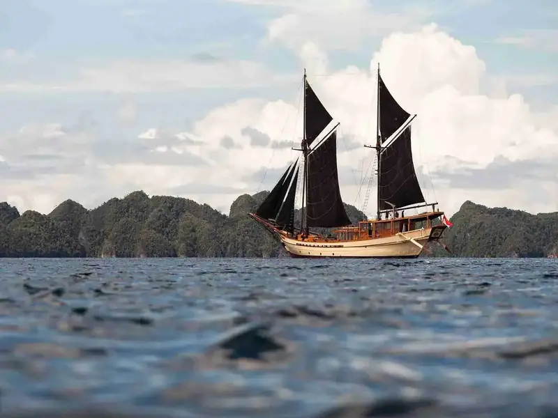Phinisi with dark sails among karst islands