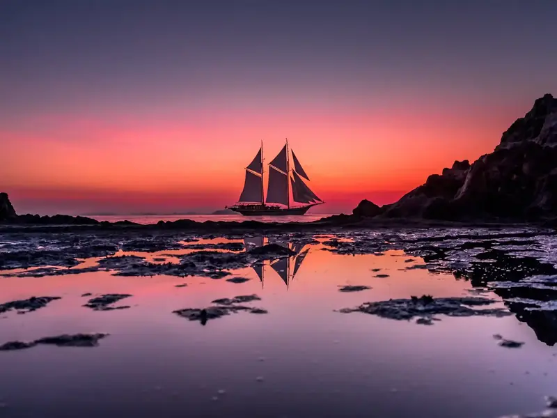 Phinisi under sail against a red sunset