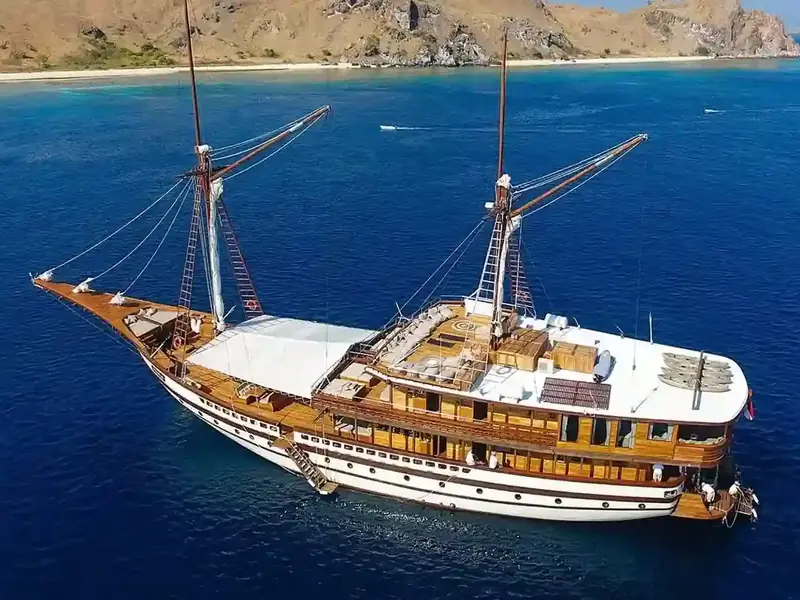 Phinisi under sail off a rugged island