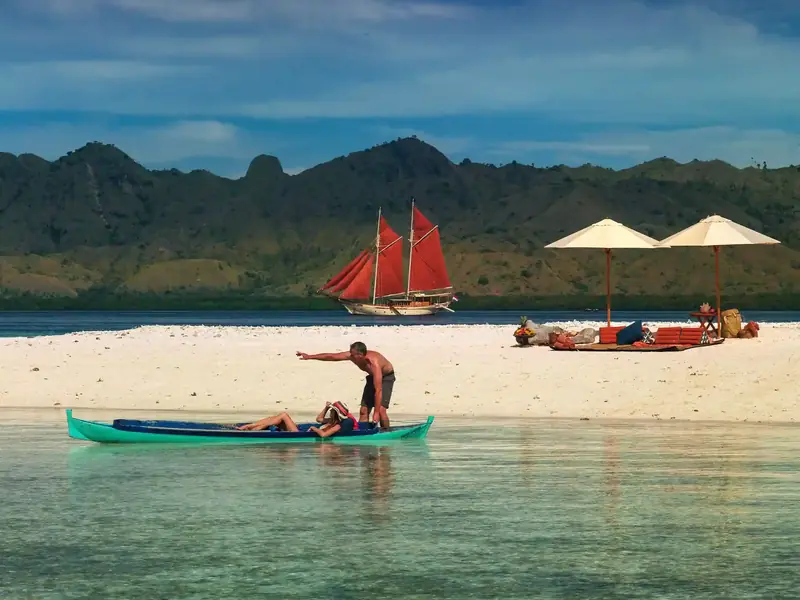 Red-sailed phinisi off a white-sand beach