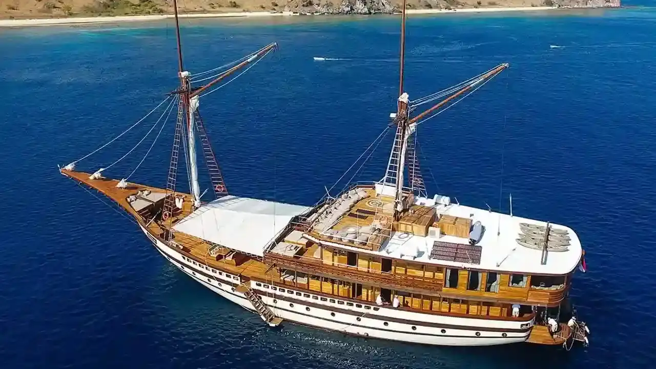 Phinisi under sail off a rugged island
